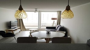 En moderne stue med et rundt spisebord, to hængende lamper, en sofa og et fjernsyn.