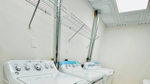Ein Waschraum mit zwei Waschmaschinen mit Frontlader, einem Wäscheständer aus Metall und einem Oberlicht.