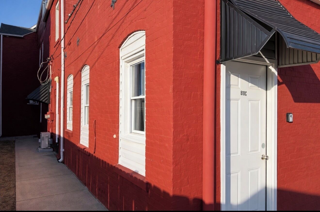 Um edifício vermelho com janelas emolduradas de branco e uma porta branca com a inscrição '810C'.