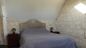 Un dormitorio con pared de piedra, cabecera de madera y cama con manta texturizada.