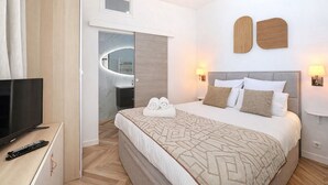 Una habitació d'hotel moderna amb un llit gran, una televisió i un bany visible a través d'una porta oberta.