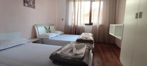 Two single beds with white mattresses and matching pillows, a small table, and a wardrobe with a mirror.