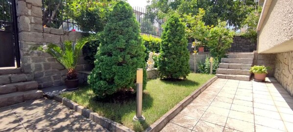 Stroll through the beautifully landscaped garden, featuring a stone pathway, potted plants, and neatly trimmed bushes.