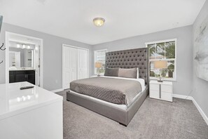 Een slaapkamer met een bed, nachtkastjes, een kaptafel en een raam met jaloezieën.