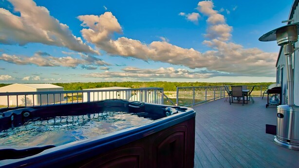 A hot tub on a wooden deck with a view of the sky and landscape.