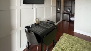 Uma sala moderna com televisão de tela plana na parede, uma mesa de jantar com cadeiras e uma cozinha ao fundo.