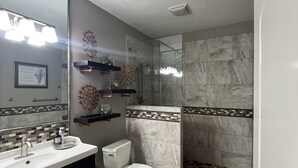 Uma casa de banho moderna com um espelho grande, sanita, lavatório e zona de duche.