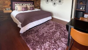 Una camera da letto con un letto, una ventola a soffitto, una parete in legno, un'opera d'arte decorativa e un piccolo tavolo con una sedia.