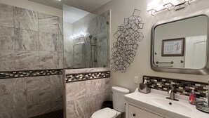 Un bagno con doccia, toilette, lavandino e uno specchio illuminato.