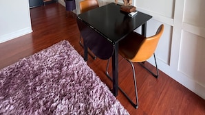 Un'area pranzo moderna con tavolo nero, due sedie, tappeto viola e televisore a parete.