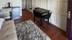 Habitación de hotel compacta con cama, kitchenette pequeña, zona de comedor con mesa y sillas, televisor de pantalla plana en la pared y alfombra estampada en el suelo.