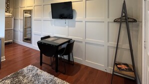 Una habitación con una televisión de pantalla plana en la pared, una mesa de comedor con sillas, una alfombra mullida y una escalera.