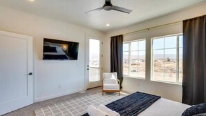 Habitación de hotel con cama, televisor montado en la pared, una silla y ventanas amplias con vistas al paisaje.