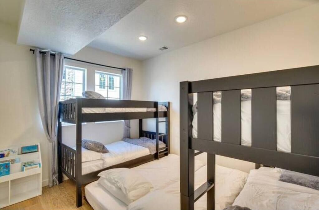 A room with bunk beds, a small white shelf with books, and a window with curtains.