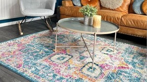 A modern living room with a blue accent wall, a white chair, a brown sofa, and a glass coffee table.