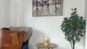 A living room with a blue sofa, a small round table with a candle, a potted plant, and a painting on the wall.