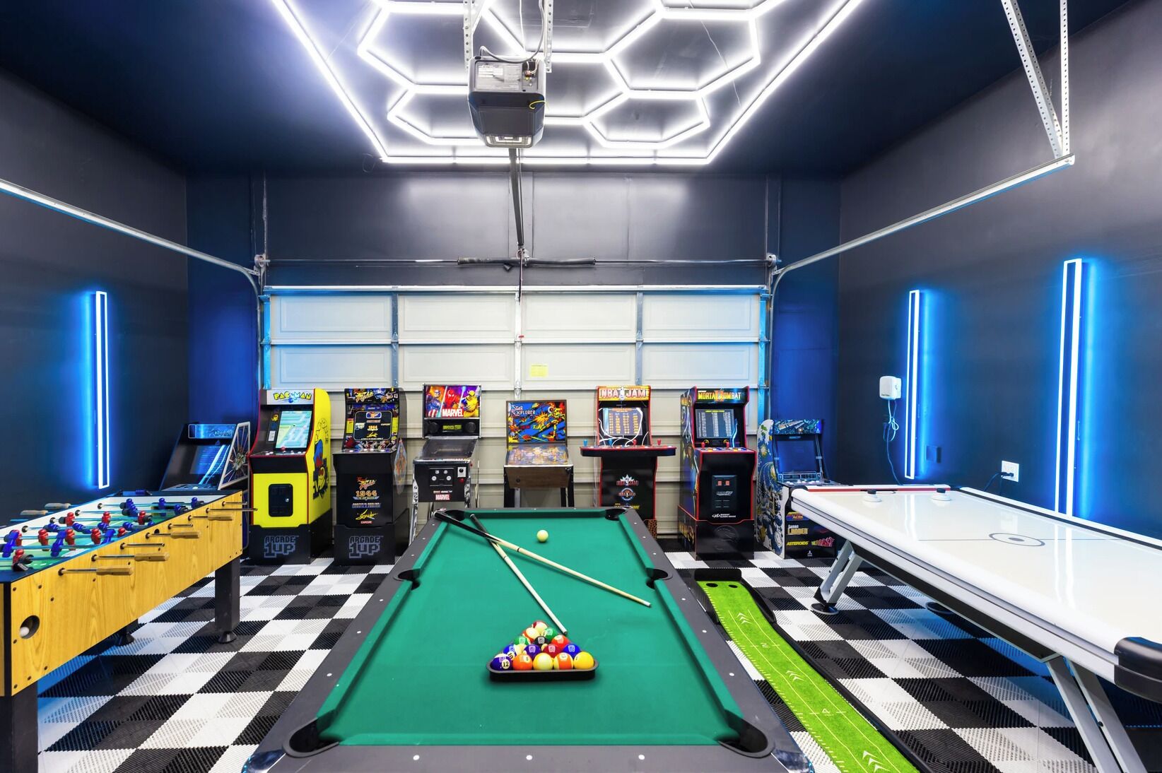 Une table de billard recouverte d’un drap de feutre vert, entourée de différents jeux d’arcade, notamment une table de baby-foot et plusieurs flippers.