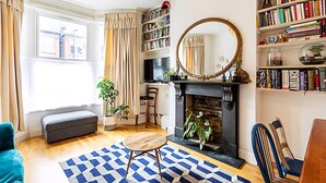 A living room with a fireplace, bookshelves, a large mirror, and a cozy seating area. - Charming Acton Dollhouse (London)