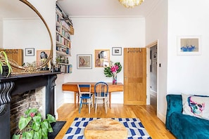 Uma sala de estar com lareira, uma mesa de jantar de madeira com cadeiras, uma estante e um sofá.
