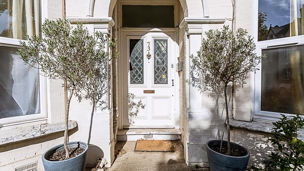 A white building with a central entrance, two potted trees, and a door with a number plate. - Charming Acton Dollhouse (London)