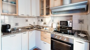 Une cuisine moderne avec des meubles blancs, un évier en acier inoxydable, un four à micro-ondes, une bouilloire et une cuisinière.