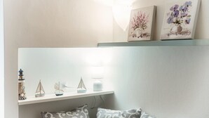 Une pièce avec un mur blanc, une étagère ornée d’objets décoratifs et une fenêtre laissant entrer la lumière naturelle.