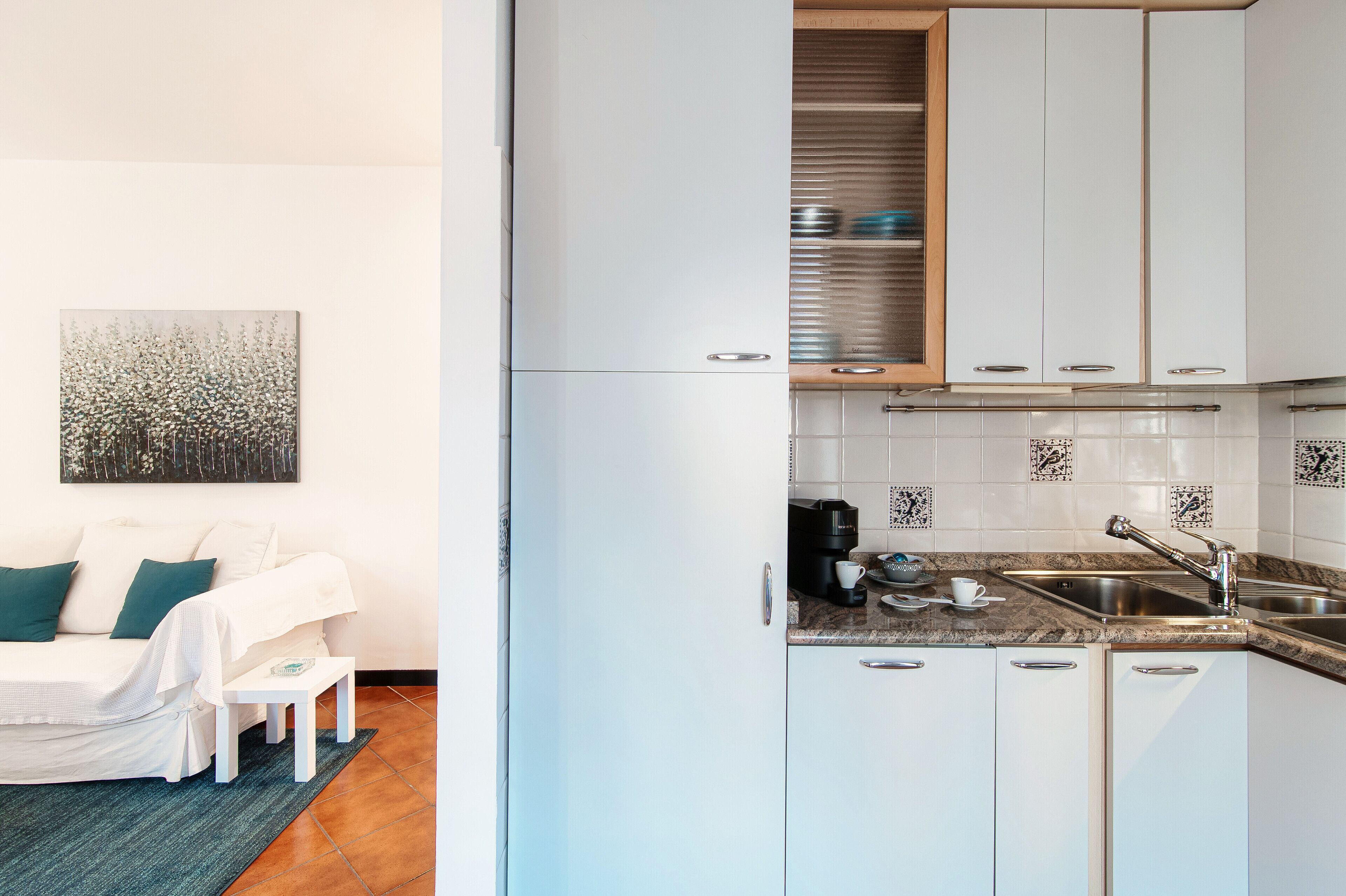 A compact kitchen with white cabinets, a coffee maker, and a sink.