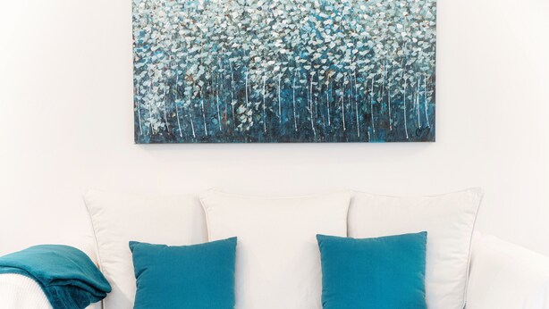 Un canapé blanc avec deux coussins turquoise et un plaid turquoise.