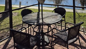 A covered outdoor seating area with a table and chairs, overlooking a body of water and trees. - Encantada Resort with lake background. (Kissimmee)