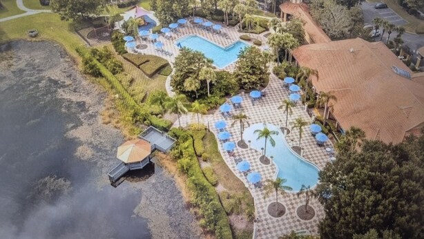 An aerial view of a resort with multiple swimming pools, palm trees, and a covered area with umbrellas. - Encantada Resort with lake background. (Kissimmee)