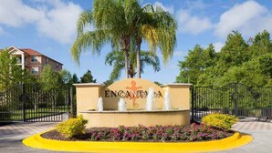 A sign with the name "ENCANTADA" surrounded by a landscaped area with a fountain, palm trees, and a yellow curb. - Encantada Resort with lake background. (Kissimmee)