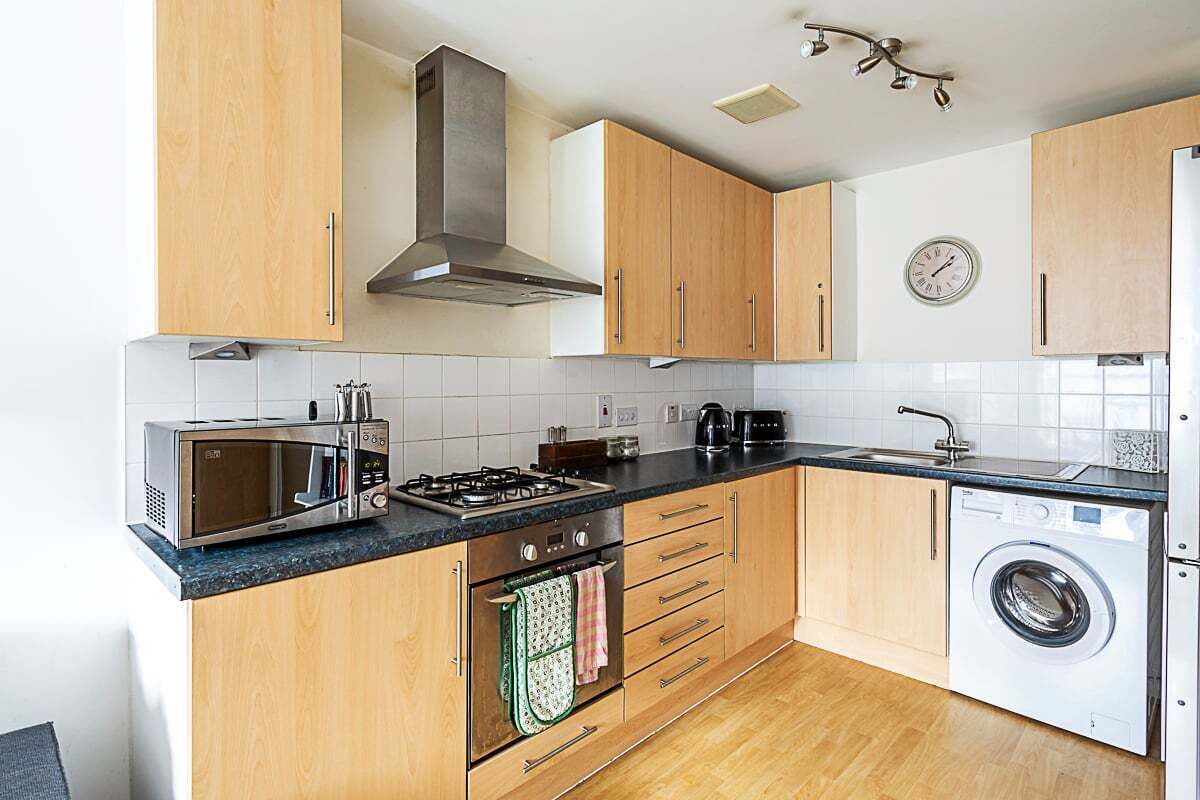 A modern kitchen with wooden cabinets, a microwave, stove, oven, and a washing machine.