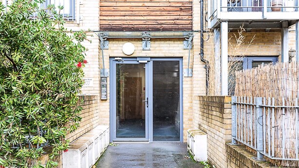 A narrow alleyway leading to a building with a wooden facade and a metal gate. - Bright Flat in Historic Whitechapel (London)