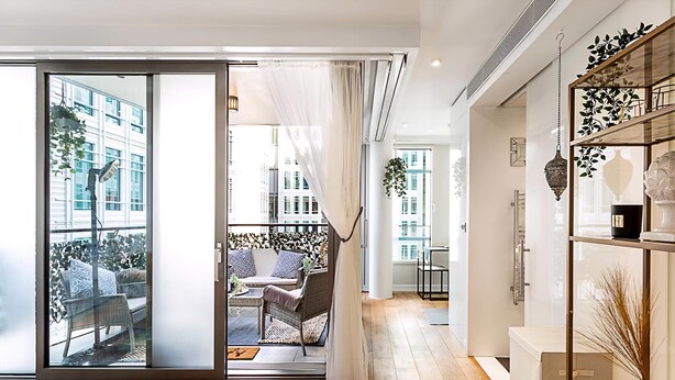 A modern interior with a sliding glass door leading to an outdoor seating area, a white console table, and a decorative plant. - Idyllic Covent Garden Flat (London)