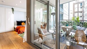 A modern interior with a bed, a wicker chair, a glass door leading to an outdoor area with plants and a table. - Idyllic Covent Garden Flat (London)