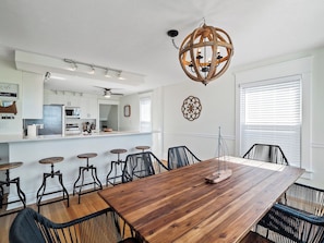 A dining area with a wooden table and chairs, a kitchen in the background, and a decorative ceiling light. - Waterfront sleeps 13 2-Kings/Crib/1st flr sleeper (Port Clinton)