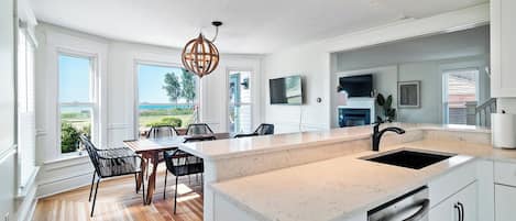 A modern kitchen with a large island, white cabinetry, and a view of the outdoors.