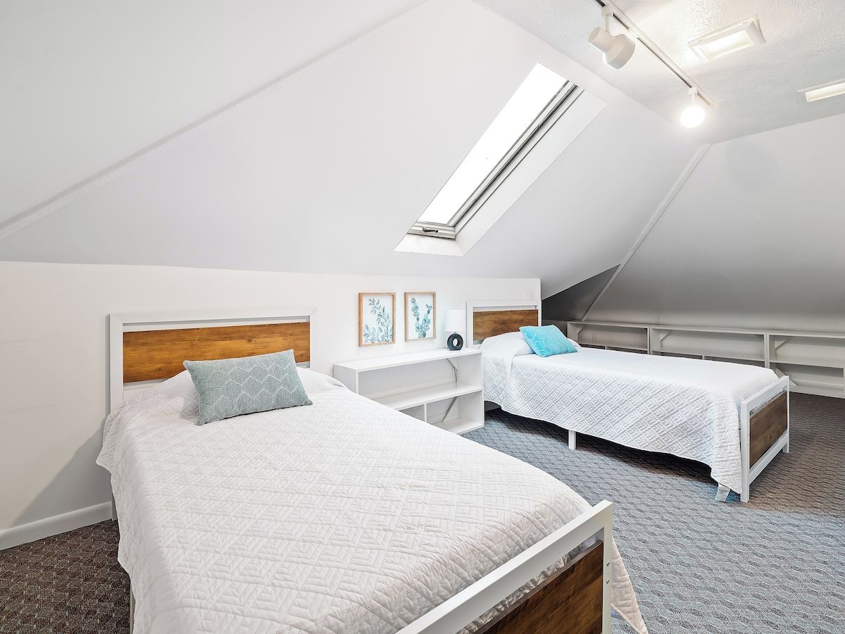 Ein Schlafzimmer mit zwei Betten, einem Dachfenster und einer weißen Farbgestaltung.