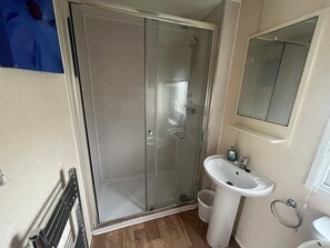 A bathroom with a glass shower enclosure, a pedestal sink, and a mirror above the sink. - Caravan - Sleeps 6 - Pets Ok - Parking (King's Lynn)