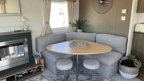 A cozy corner seating area with a round table, grey upholstered sofas, and a small bar stool. - Heacham Beach Coastal 2 Bedroom Chalet Retreat (King's Lynn)