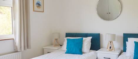 A bedroom with two beds, a round mirror, and a window with curtains.