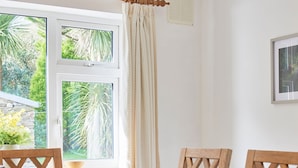 Un comedor con una mesa de madera, cuatro sillas, un tazón y una ventana con cortinas.