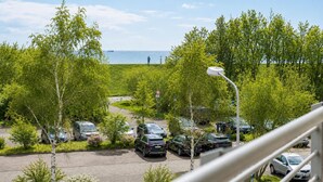 A parking area with cars, trees, and a view of the sea. - Kurpark- Residenz App. 217 Seesicht, Kurparkallee 47, 27476 Cuxhaven- Döse (Cuxhaven)