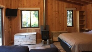 Une cabane en bois avec un lit, un banc, une cheminée et un téléviseur.