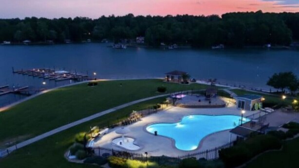 A large outdoor swimming pool surrounded by a well-maintained lawn, with a dock and boats in the background. - Blue Ridge Sanctuary: Luxury Retreat at SML (Huddleston)