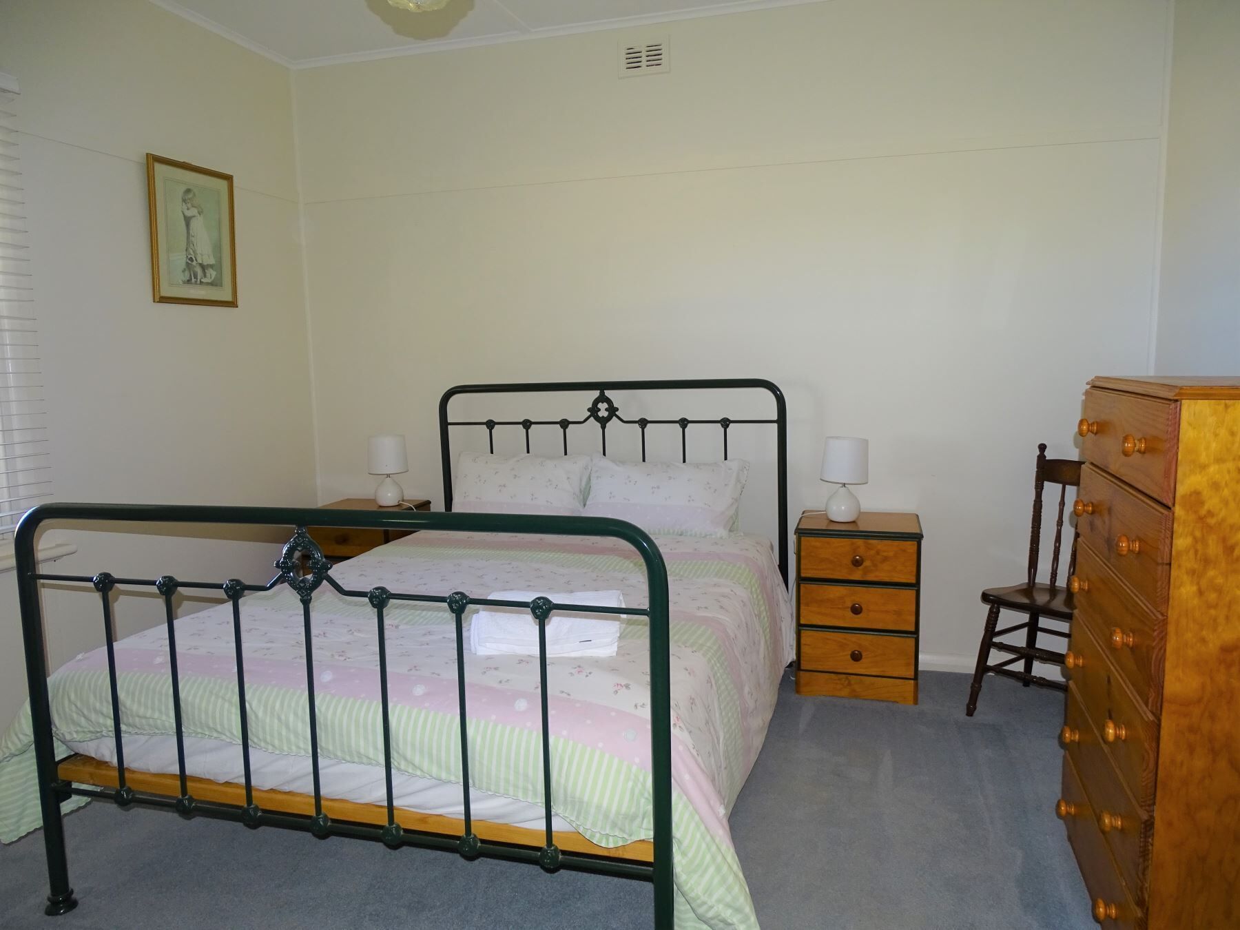Une chambre à coucher avec un lit en métal, une commode en bois, une table de chevet et une chaise.