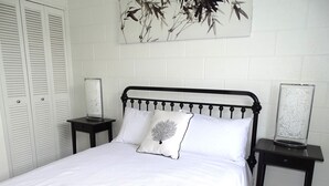 A neatly made bed with white bedding and a single decorative pillow, flanked by two bedside tables with lamps, against a white brick wall. - Hamptons, Port Vincent (Port Vincent)