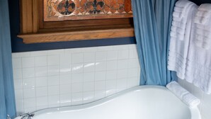 Un baño con una bañera blanca, cortinas azules y un panel decorativo de azulejos sobre la bañera.