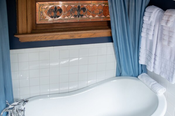Un baño con una bañera blanca, cortinas azules y un panel decorativo de azulejos sobre la bañera.
