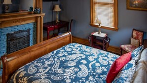 Un dormitorio con una cama de madera, chimenea, escritorio y una silla.